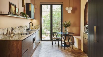 A kitchen with open shelving as well as a worktop and sink. There is also a section with a dining table and chairs as well as a vase and flowers on top of the table