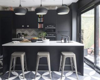 A matt black kitchen with petal motif floor tiles and zig-zag white and grey backsplash