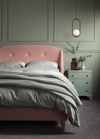 A sage green bedroom with a pink studded wingback bedframe and grey bedding