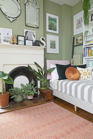 Guest bedroom/office with green painted walls, grey day bed, red and white rug and gallery wall of prints and mirrors