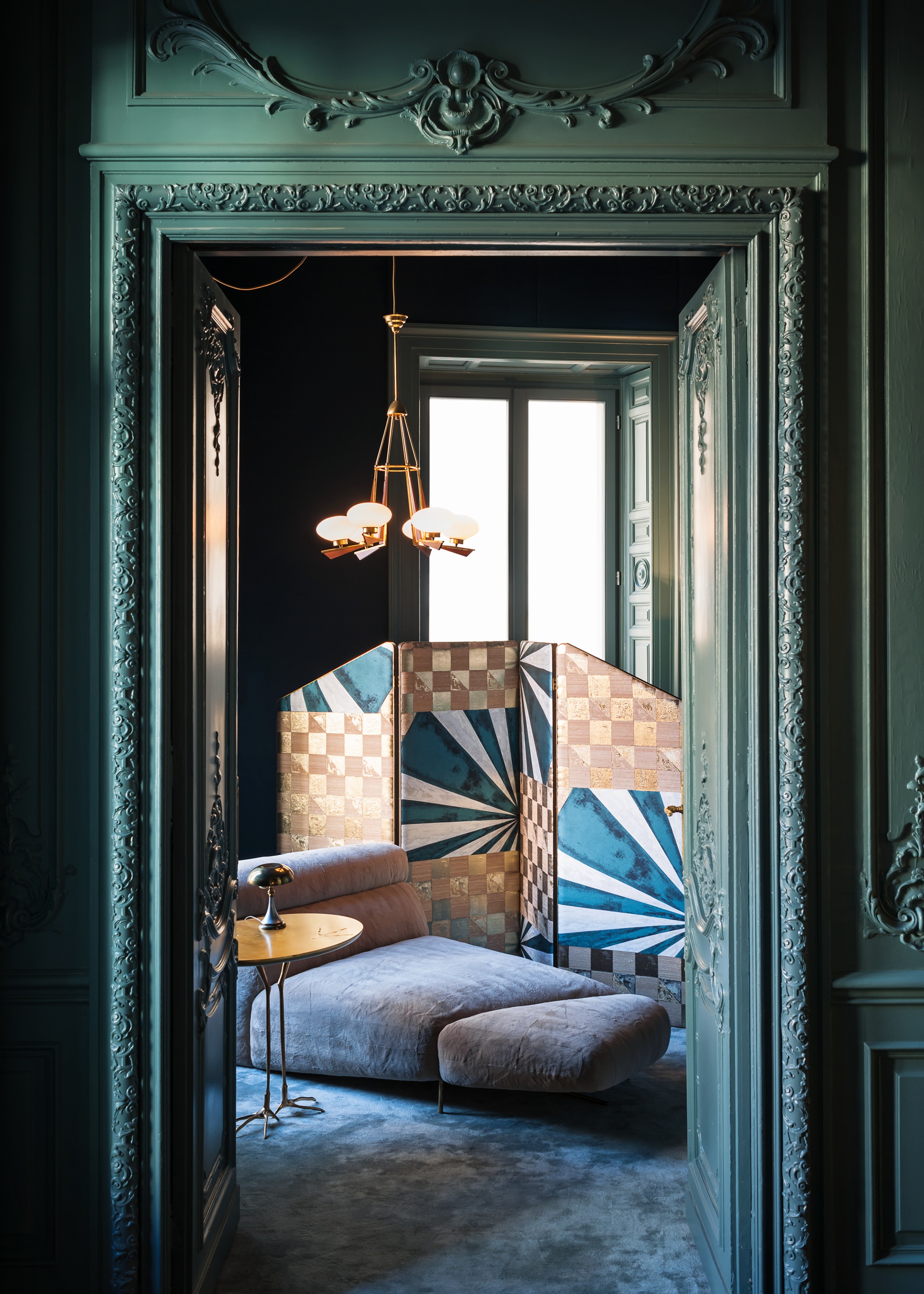 a view through a green doorway into a room with a chaise lounge and folding screen