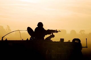 Silhouette of an army soldier preparing his tank and weapons at sunset 
