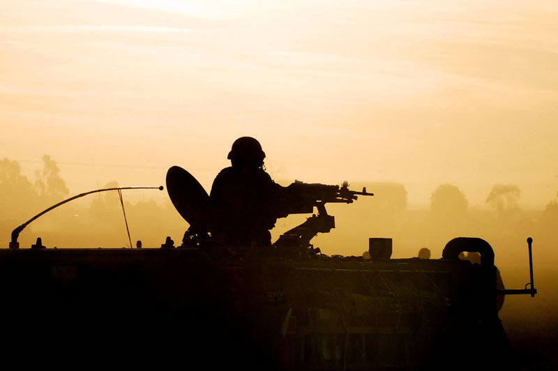 Silhouette of an army soldier preparing his tank and weapons at sunset 