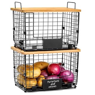 Two black wire baskets with wooden lids stacked on top of now another. The bottom basket holds potatoes and red onions