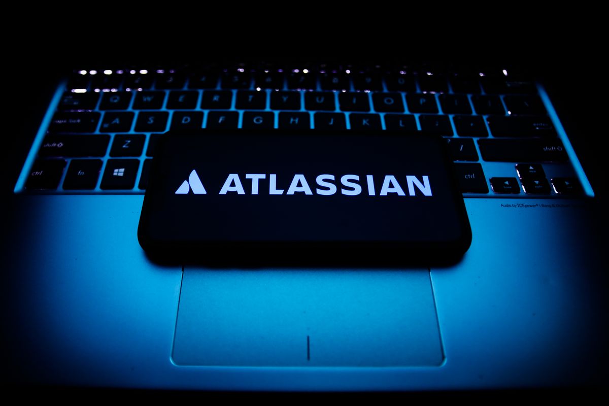 Atlassian logo displayed on a phone screen and a laptop keyboard are seen in this illustration