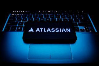 Atlassian logo displayed on a phone screen and a laptop keyboard are seen in this illustration