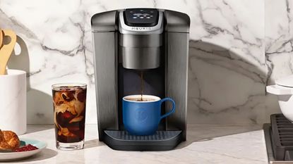 One of the best Cyber Week Keurig deals: Keurig K-Elite on a marble countertop with iced coffee and a croissant beside it