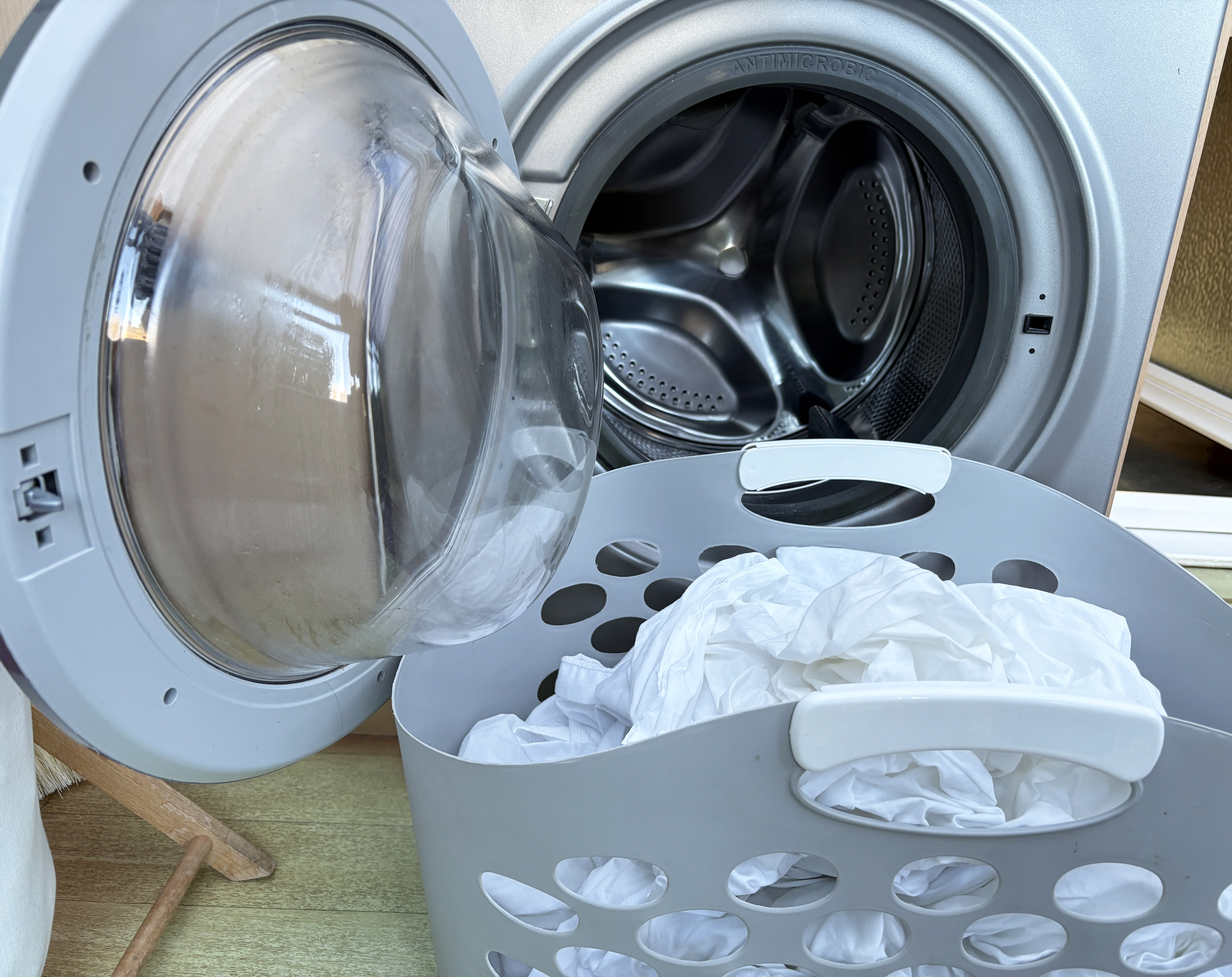 A tumble dryer with the door open and a laundry basket with clean washing in