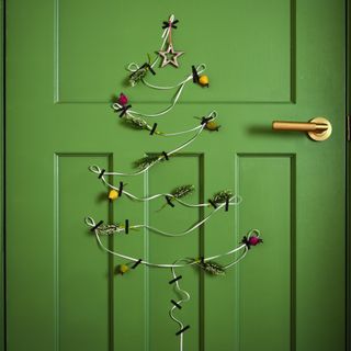 A green door with a Christmas tree design made out of ribbon, tape and berries