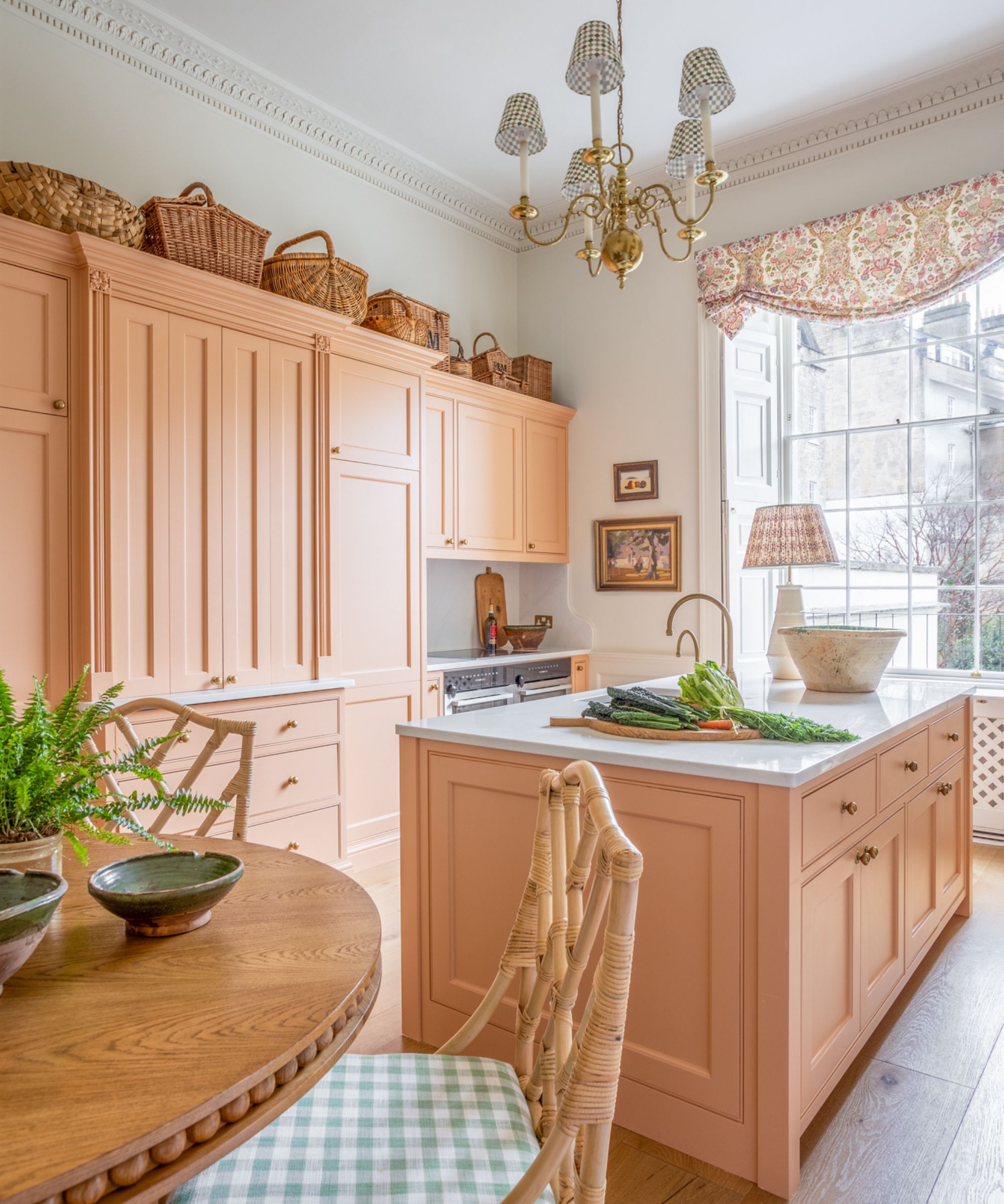 A traditional kitchen with peach pink cabinetry and island, white walls, and baskets along the top of the wall cabinets