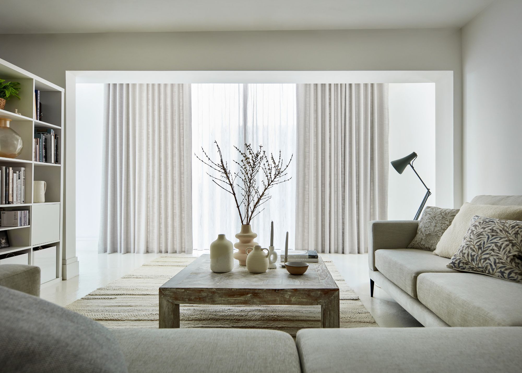 A modern white living room with neutral decor and sliding glass doors with sheer curtains and a heavier neutral curtain.