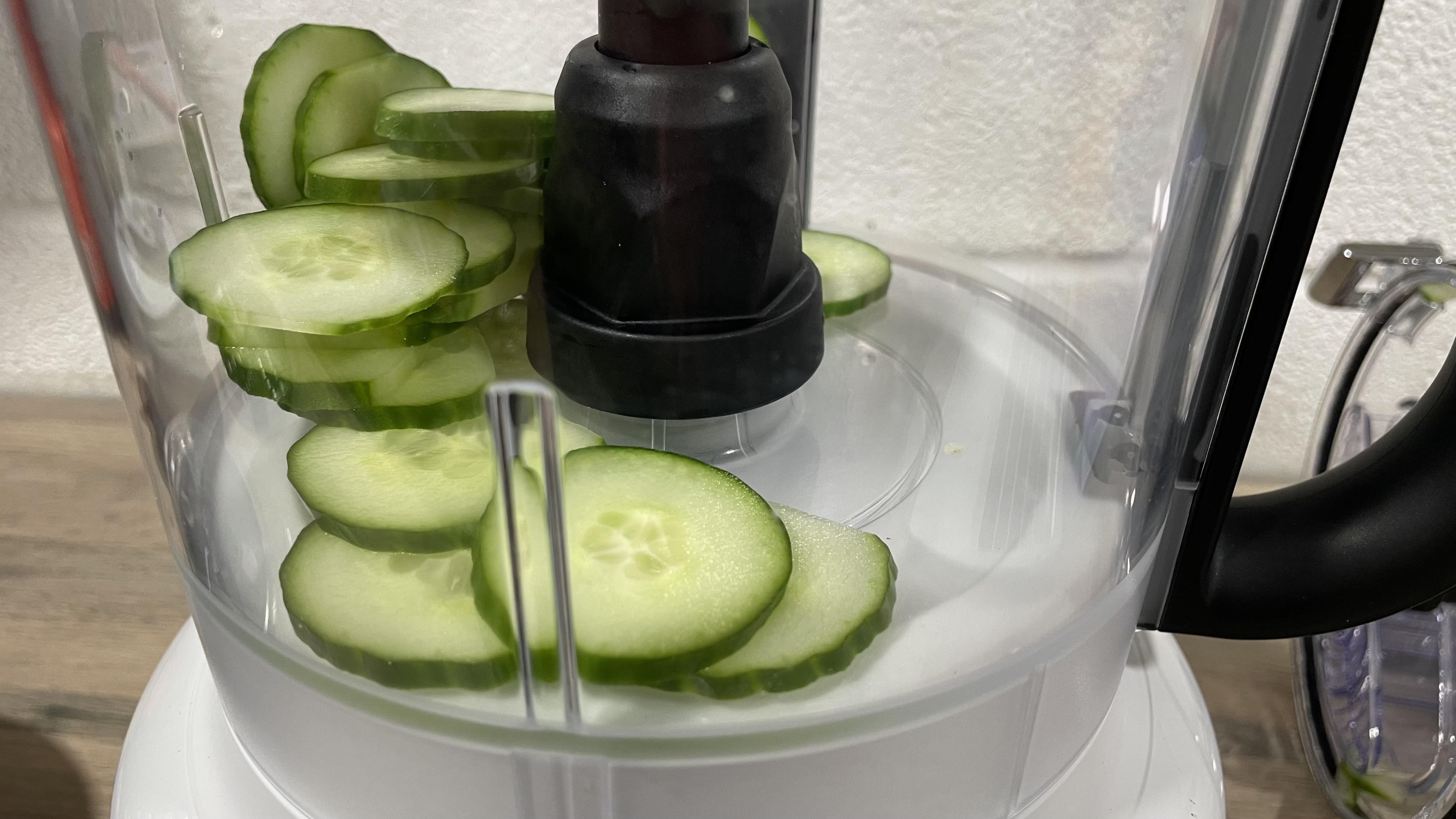 A close up photo of neatly sliced cucumber inside the KitchenAid 13 cup food processor work bowl.