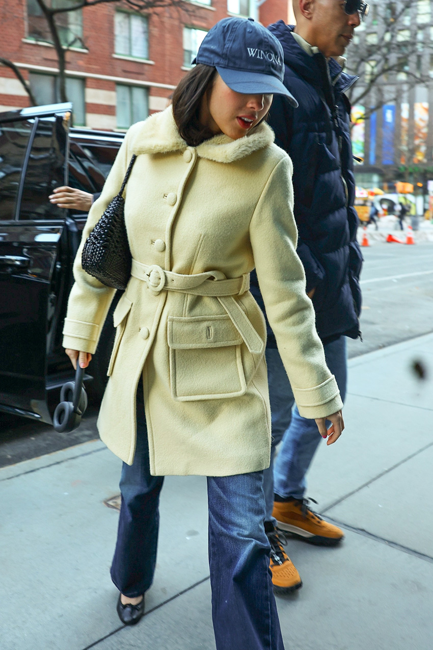 Olivia Rodrigo wearing a baseball cap, yellow coat, bootcut jeans, and ballet pumps in NYC