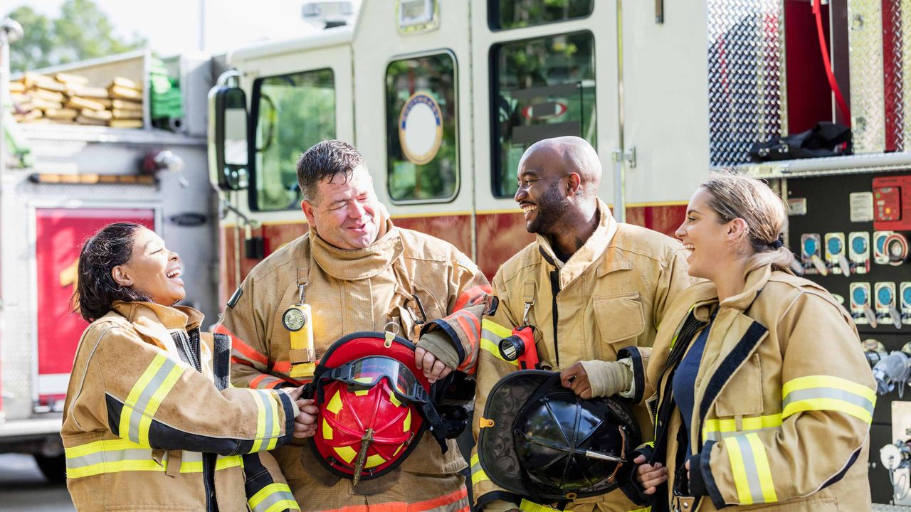 Four firefighters chat in front of a fire truck.