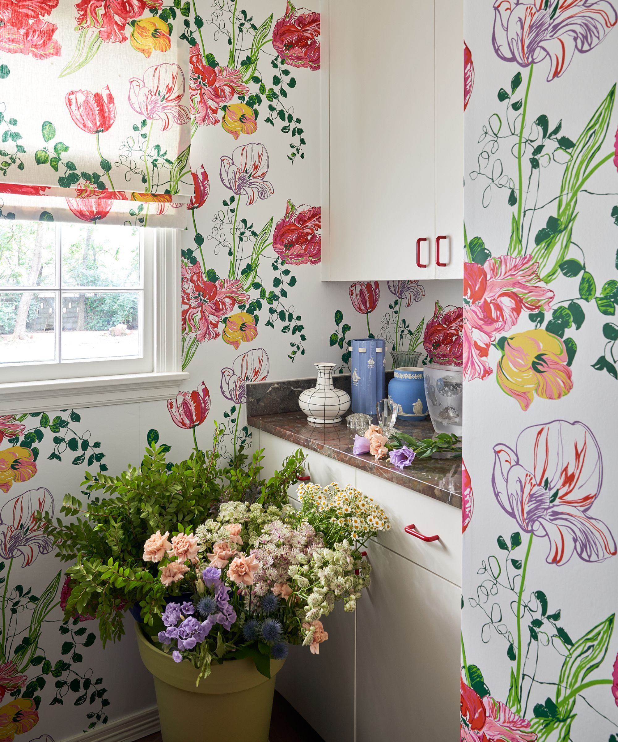 a wallpapered laundry room with tulip floral wallcovering, white cabinetry and filled with buckets of fresh cut flowers