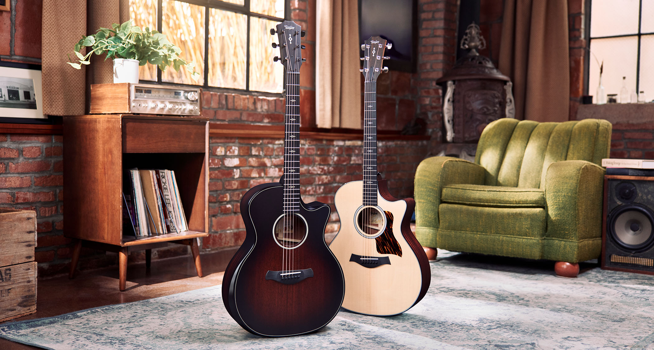 Taylor Next Generation Grand Auditorium: the two refreshed cutaway electro-acoustic guitars are photographed in front of a green sofa and a vintage hi-fi unit.