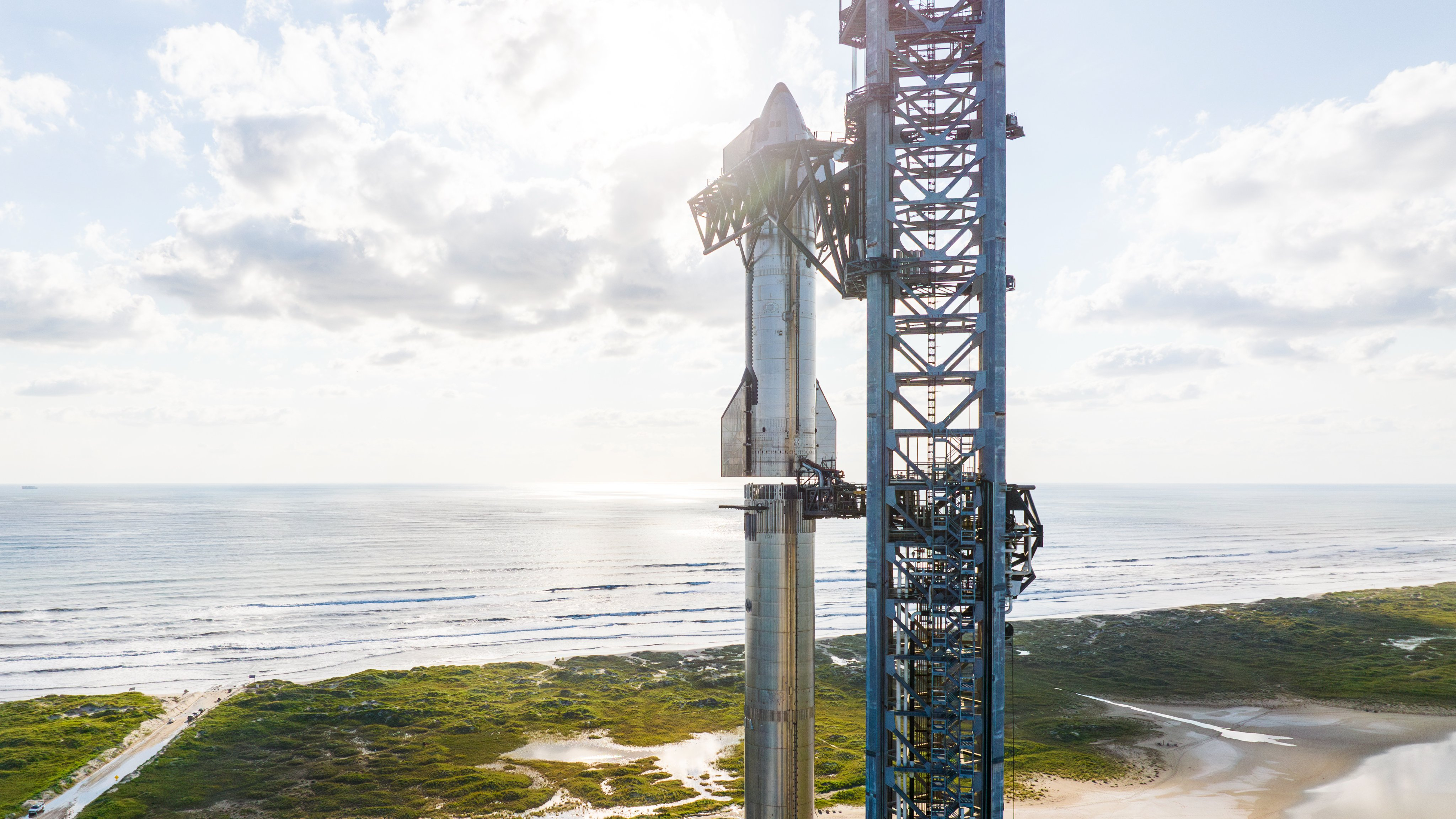 거대한 은색 우주선 로켓이 SpaceX의 Flight 5의 해변 발사대 위에 있는 거대한 부스터 위에 쌓여 있습니다. 은색 SpaceX 우주선 로켓이 부스터 위에 올려져 있습니다.