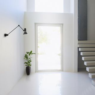 White hallway with open door, staircase and black wall light