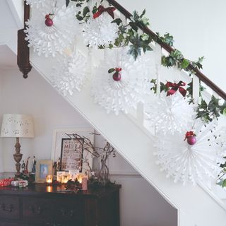 A Christmas-decorated hallway with a staircase adorned with fan paper decoratings and red bows