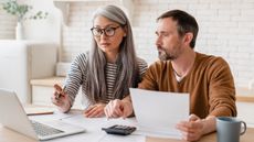 A couple go over their debt together while sitting at their table and looking at a laptop.