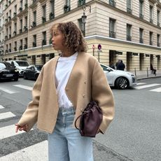 Ellie Delphine in a double-breasted jacket, T-shirt, jeans, and a burgundy clutch.