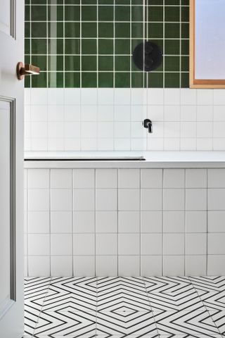 Bathroom with monochrome pattern floor tile, white square tiles up bath, and deep green square tiles on wall