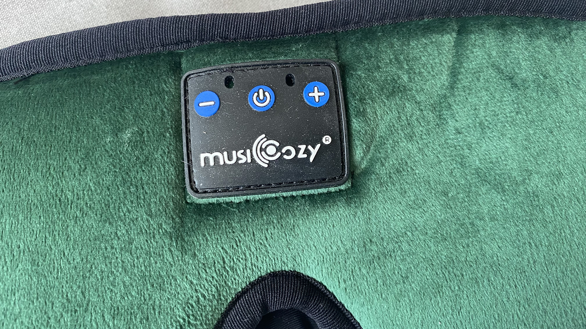 A closeup of the control panel on the front of the MUSICOZY Bluetooth sleep eye mask. There are three small buttons; a plus sign, a power on / off, and a minus sign