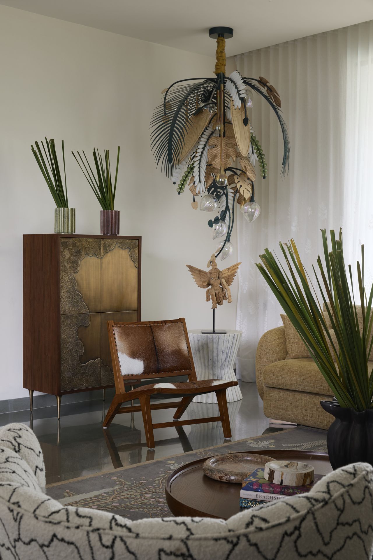 A living room with a feather-like lighting piece, a leather-upholstered chair and a brass console