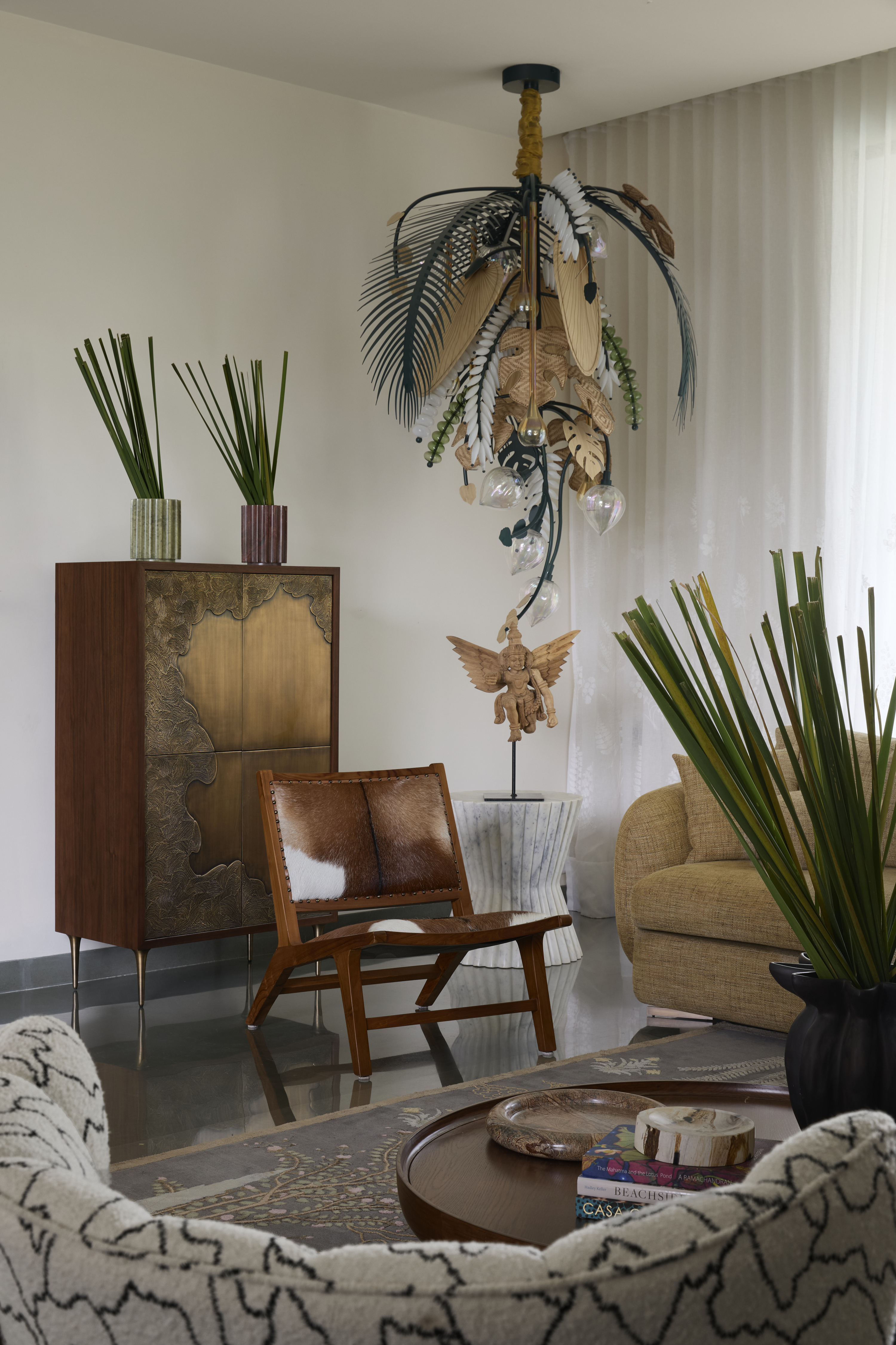 A living room with a feather-like lighting piece, a leather-upholstered chair and a brass console