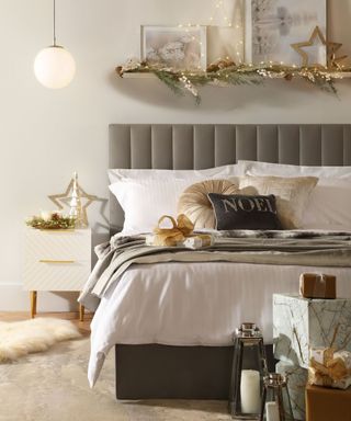 A neutral bedroom with a grey padded headboard, and black and gold christmas decor and pillows