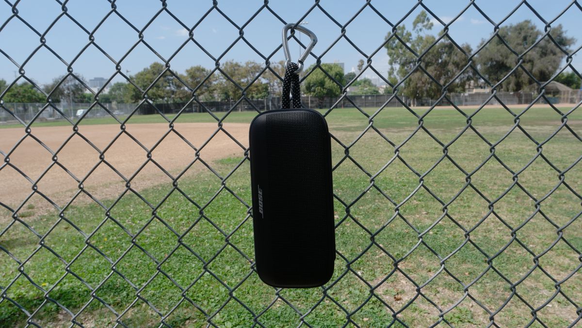 Bose SoundLink Plus hanging from a fence from the rugged nylon carry loop and a carabiner