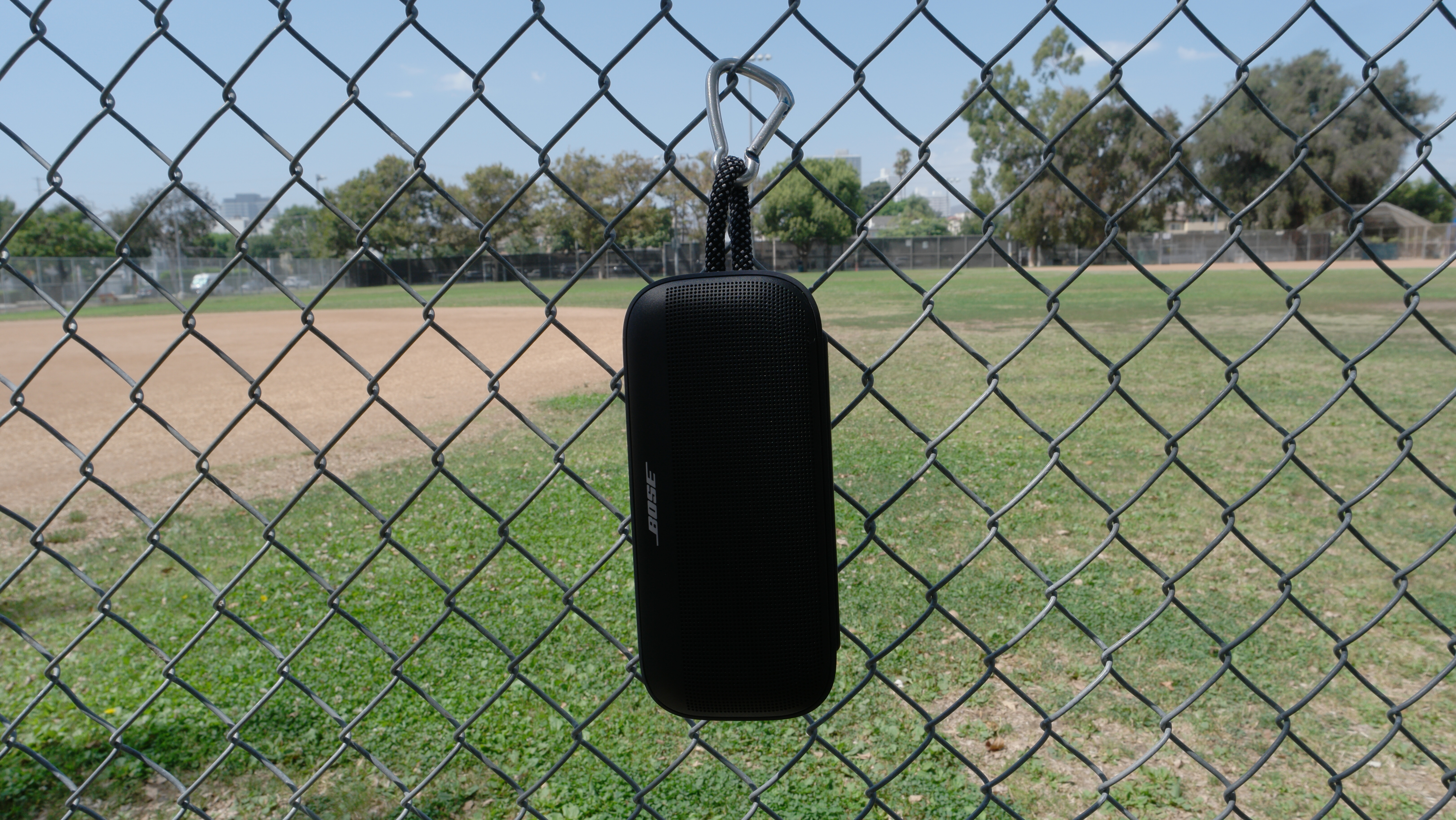 Bose SoundLink Plus hanging from a fence from the rugged nylon carry loop and a carabiner