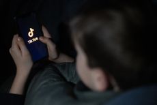 A 12-year-old boy looks at a smartphone screen displaying the TikTok logo