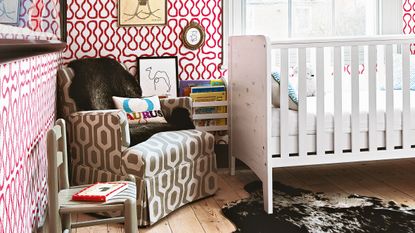 Gender neutral nursery ideas featuring red and white wallpaper, a white painted crib and brown armchair.