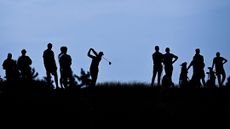 A group of silhouetted golfers watching one tee off