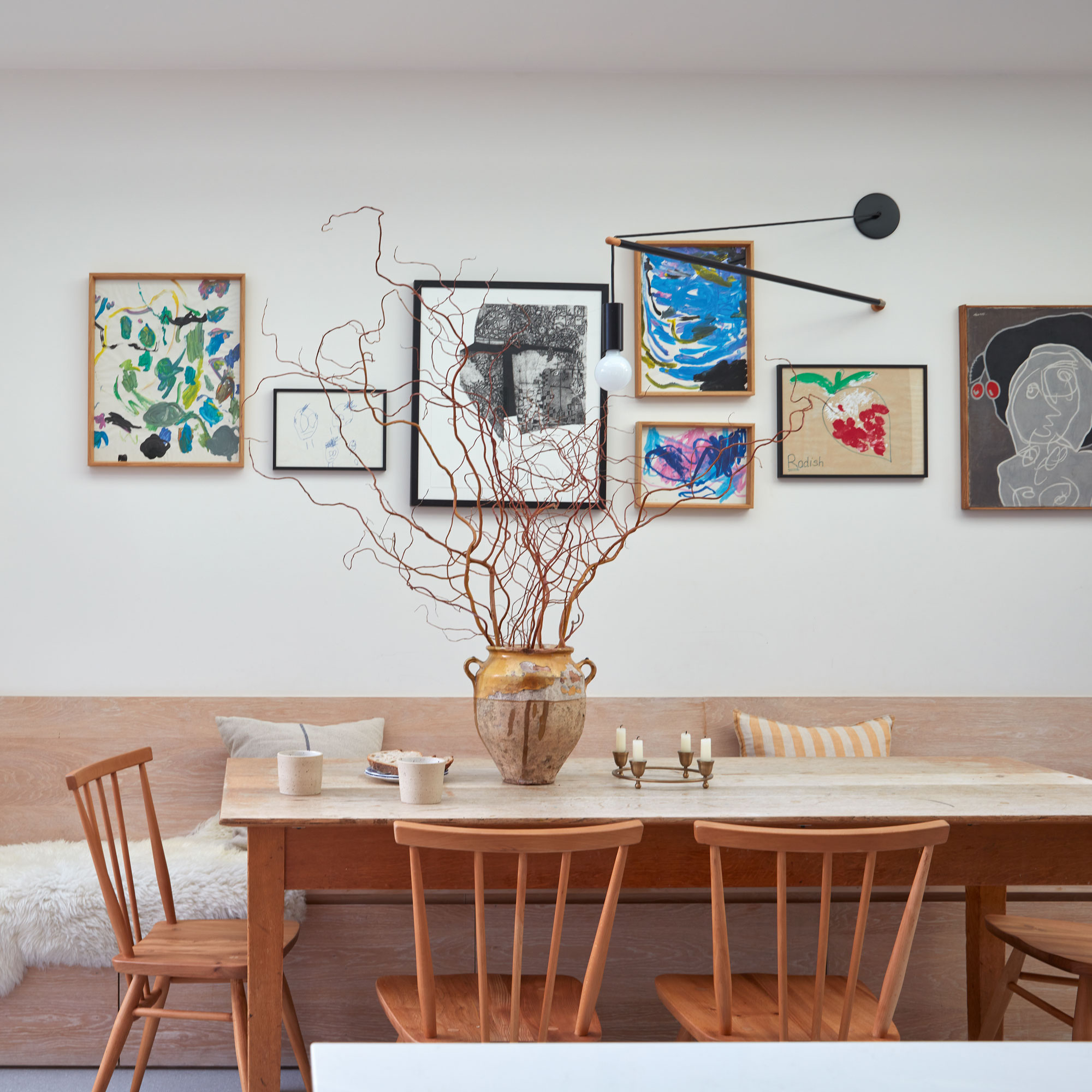 White dining area with wooden table and chairs, gallery wall, lamp and ceramic vase