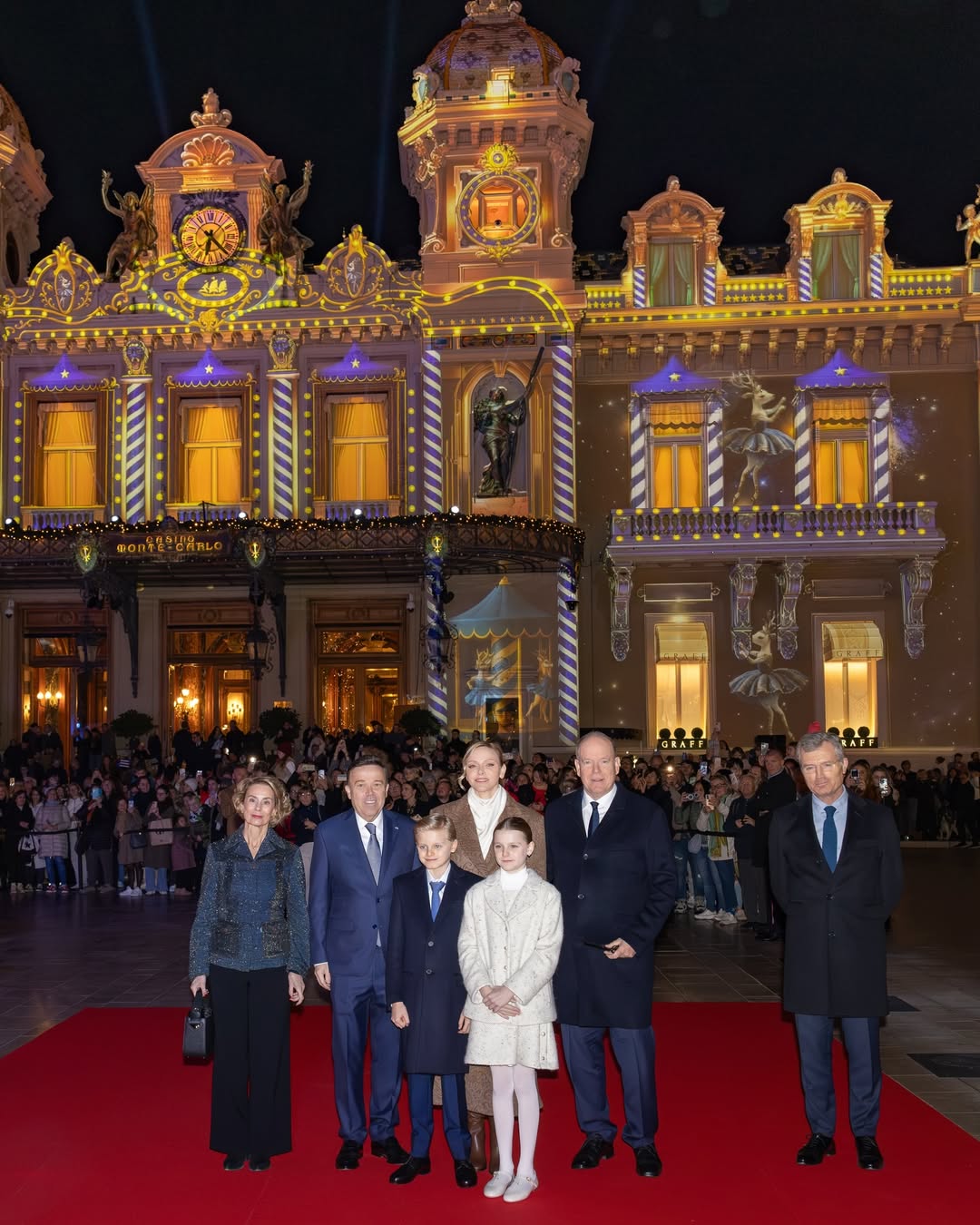 Princess Charlene, Prince Albert, Prince Jacques and Princess Gabriella in front of a lit up building with Christmas lights