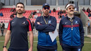 Roy Kent, Coach Beard, and Ted Lasso stand on the side of the pitch in Ted Lasso