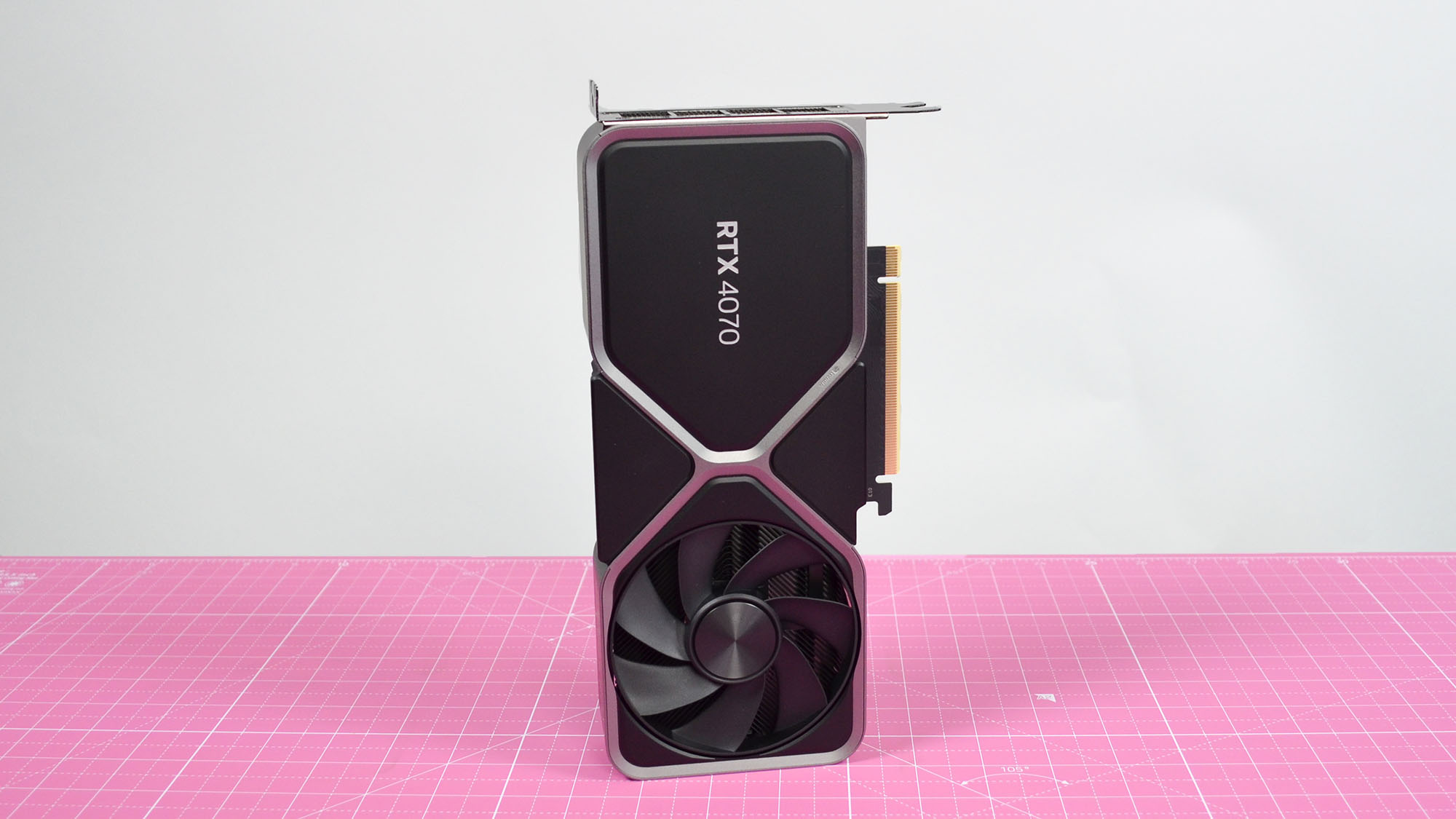An Nvidia GeForce RTX 4070 graphics card standing upright on a pink desk mat