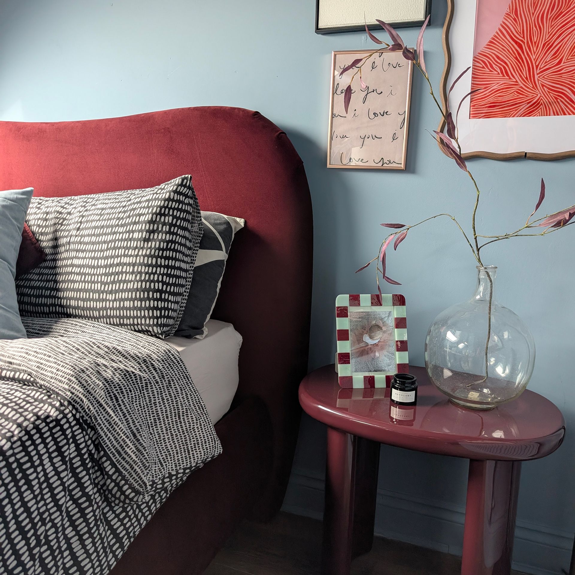 Blue bedroom with burgundy bed and bedside table, monochrome bedding, framed prints on wall