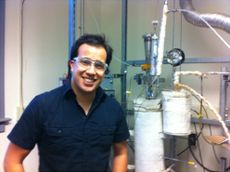 Robert Coolman, wearing a blue shirt and a lazy smile, stands in front of the biofuels reactor he built.