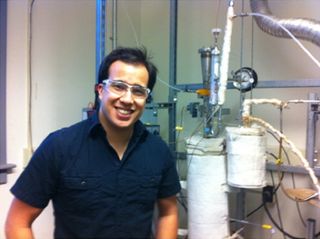 Robert Coolman, wearing a blue shirt and a lazy smile, stands in front of the biofuels reactor he built.