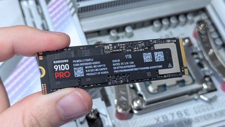 A hand holds a Samsung 9100 PRO M.2 SSD above an open computer motherboard, highlighting the storage upgrade in a clean, technical setting.