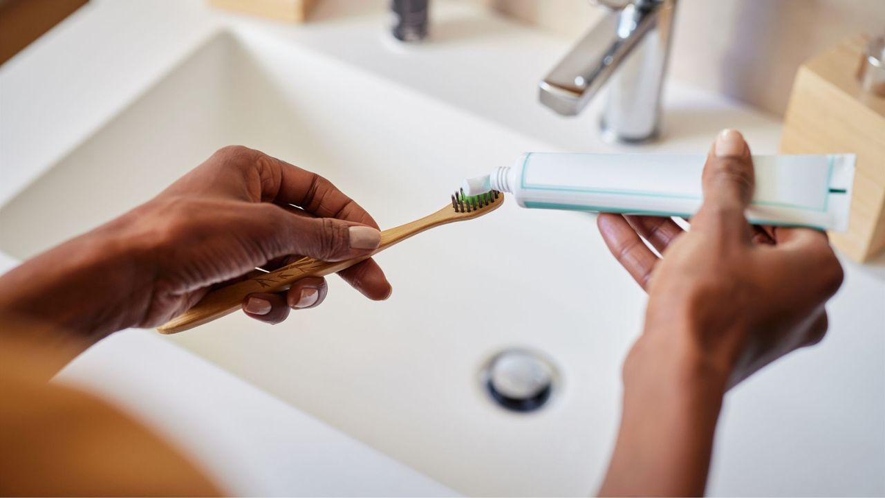 Woman putting toothpaste for sensitive teeth onto a soft bristle toothbrush in bathroom, representing question why are my teeth so sensitive