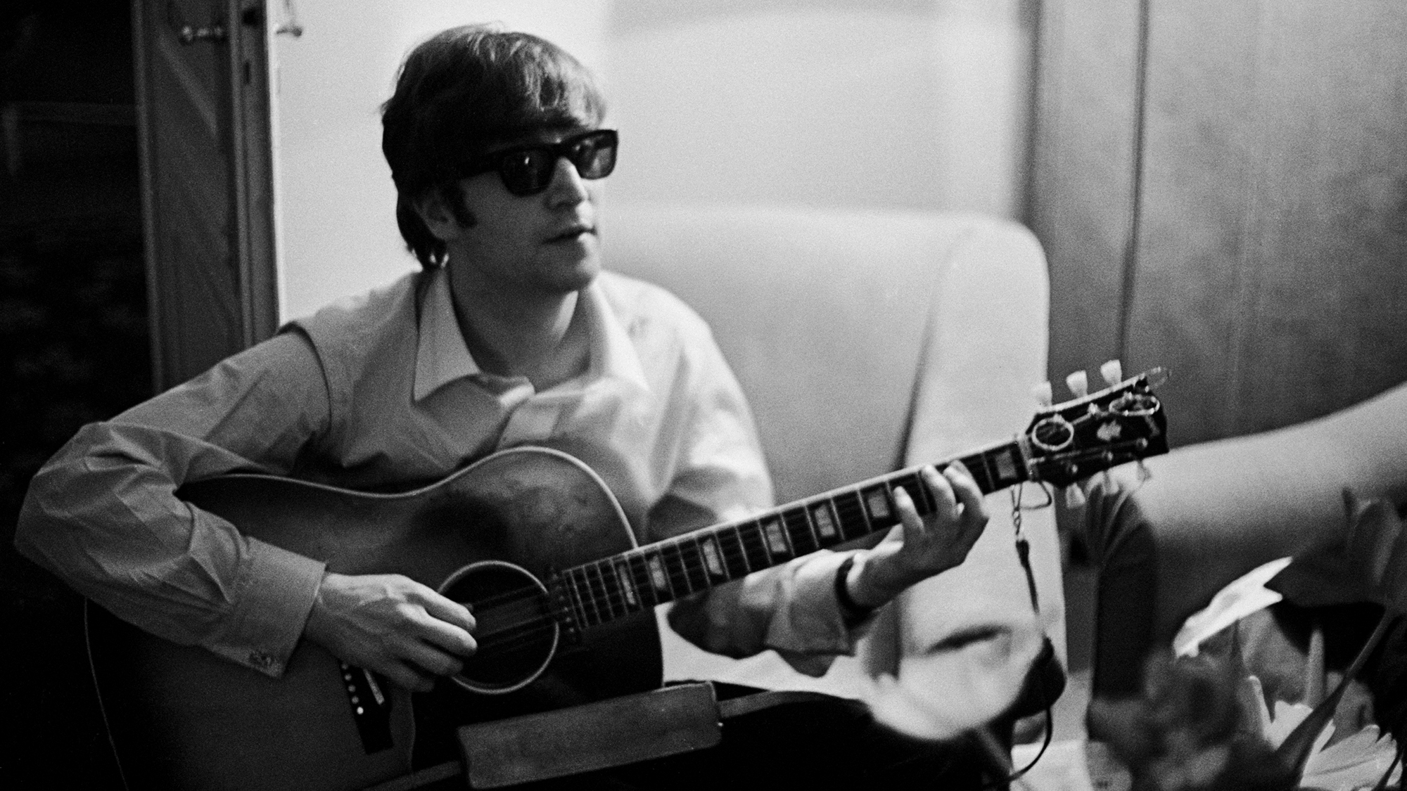 John Lennon plays the guitar in a hotel room in Paris, 16th January 1964.