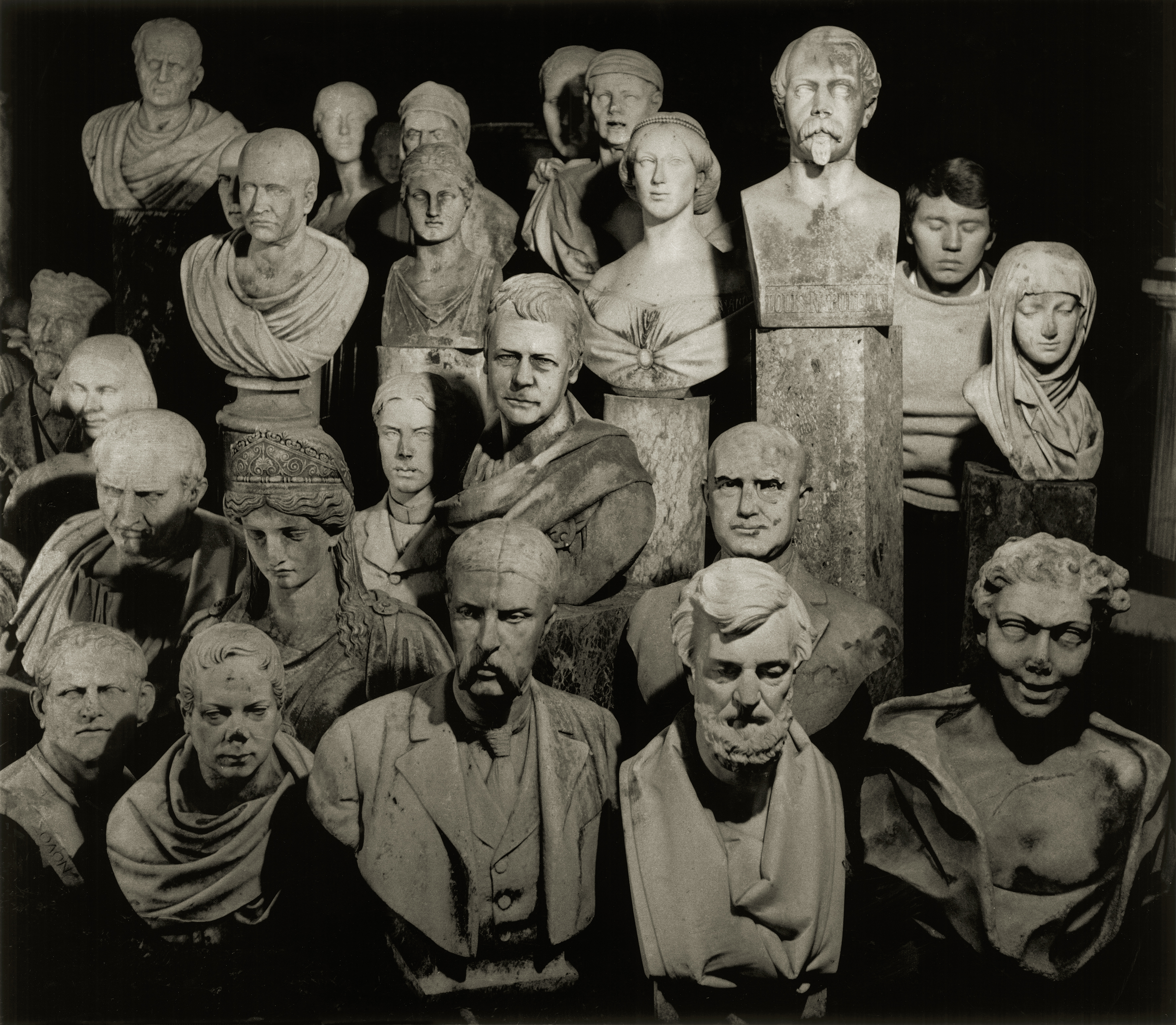 Don McCullin&rsquo;s face is partially hidden as he blends into a dense, atmospheric arrangement of historical stone busts and sculptures.