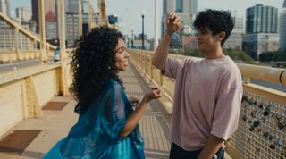 a couple (eva reign as kelsa and abubakr as khal) stand on a bridge, as khal (right) holds a lock with "K + K" drawn on it, in the prime video rom-com 'anything's possible'