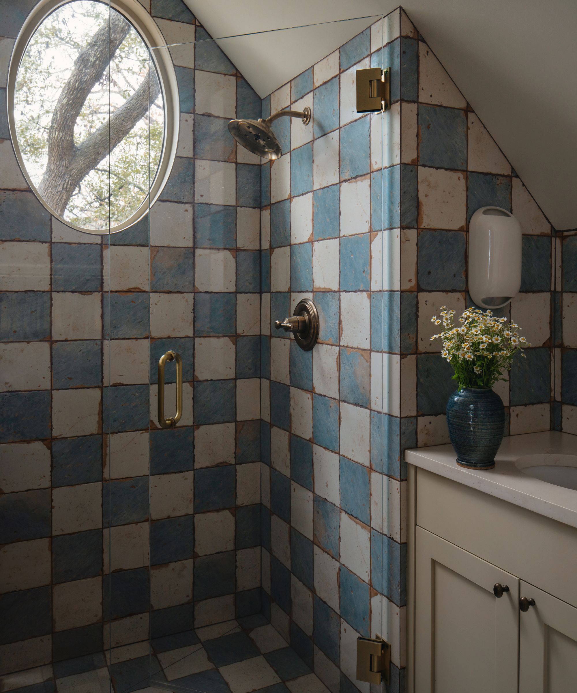 blue and white checkerboard tiled shower with an oval window and brass hardware