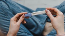 young woman sitting on the bed and holding a positive pregnancy test