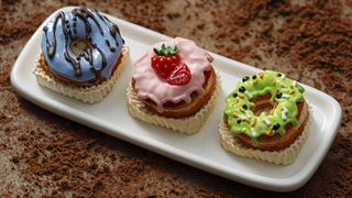 A set of three artisanal keycaps depicting sweet treats, on a white tray